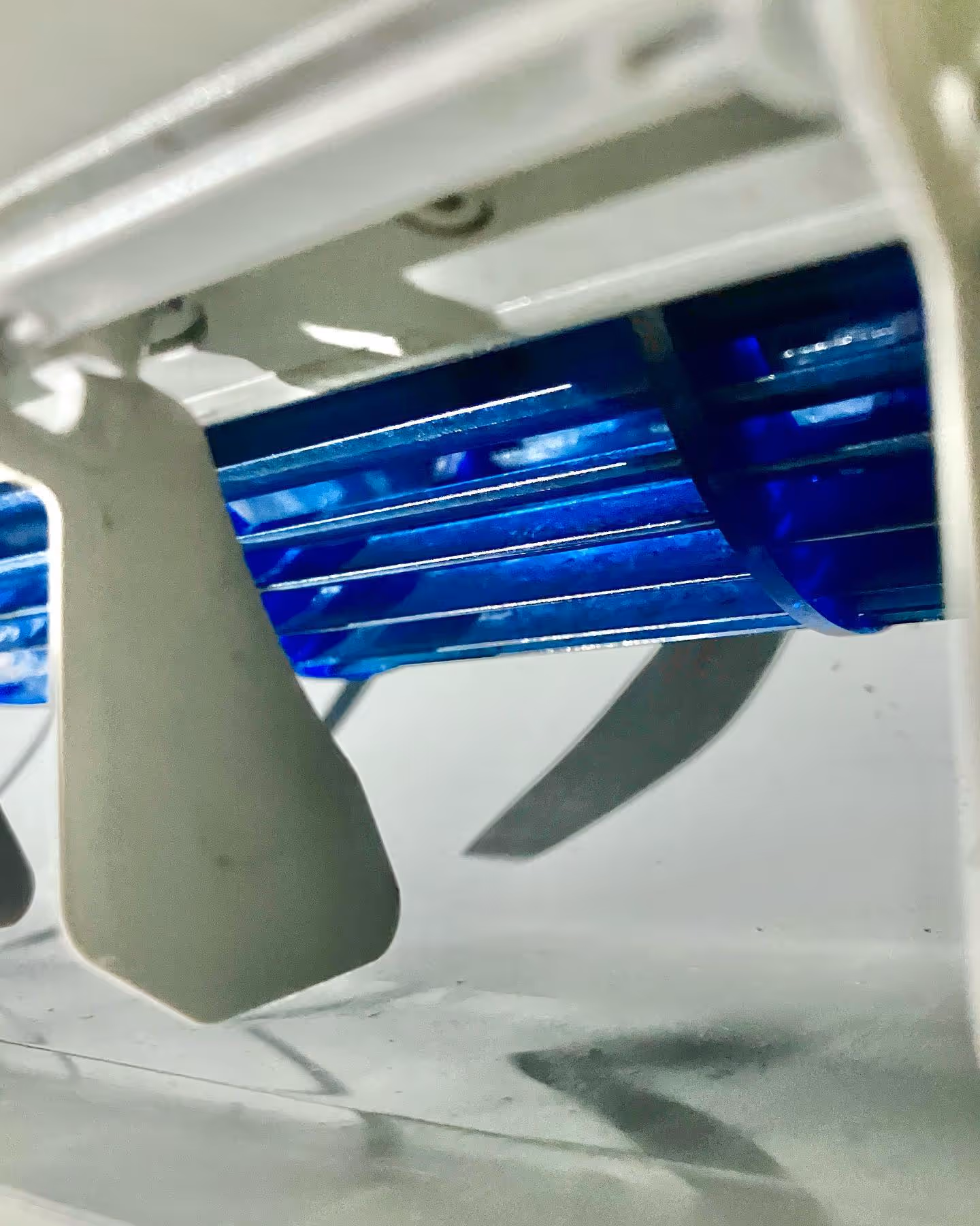 Close-up of white plastic adjustable vent fins with blue cylindrical fan blades behind them.