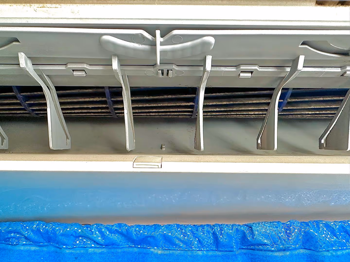 Close-up of a dusty air conditioning vent above a blue fabric surface.