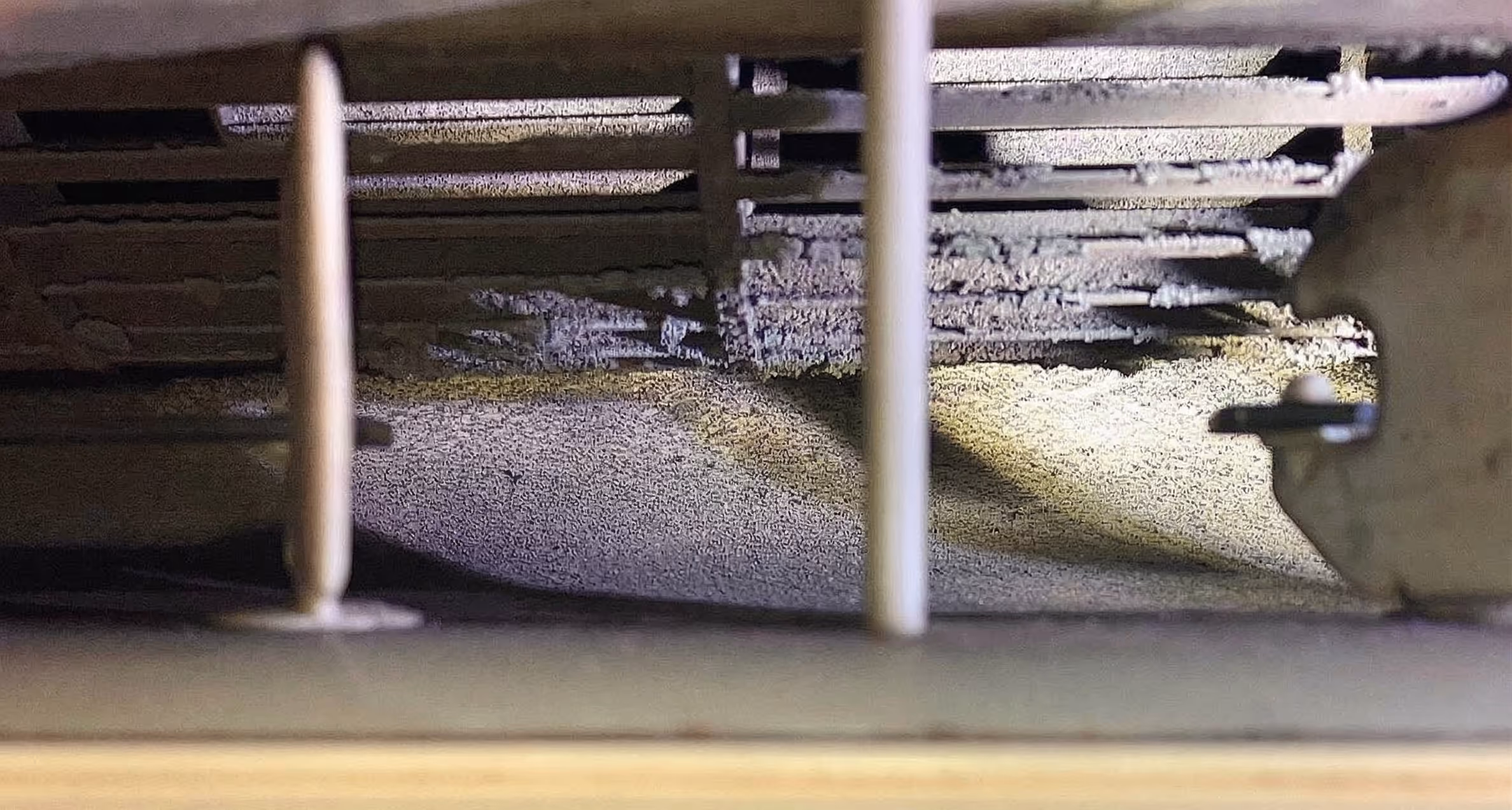 Close-up view inside a metallic compartment showing dust buildup and structural rods.
